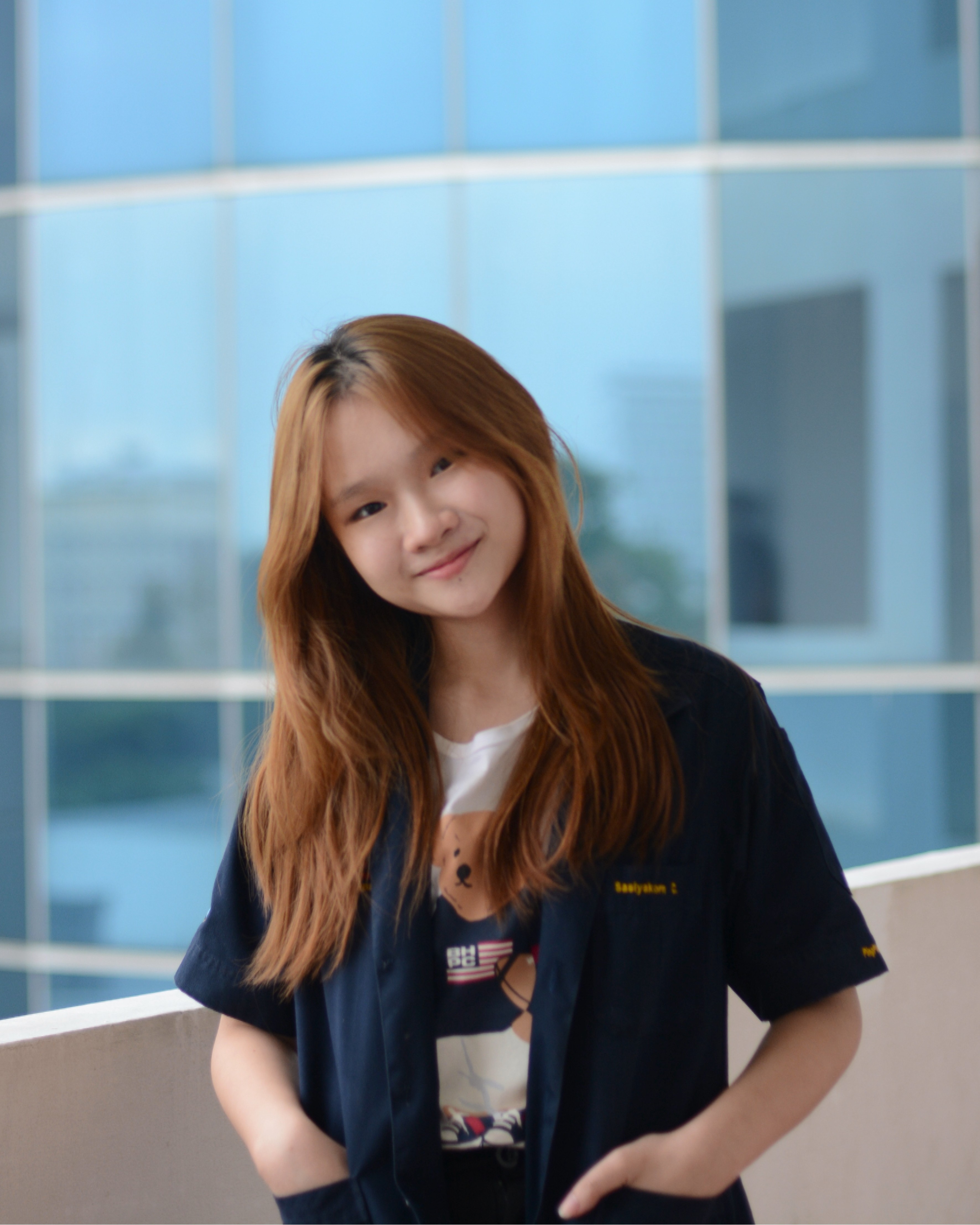 Sasiyakorn Chansiri smiling at the camera, wearing a black t-shirt and standing in front of a white wall with a window.